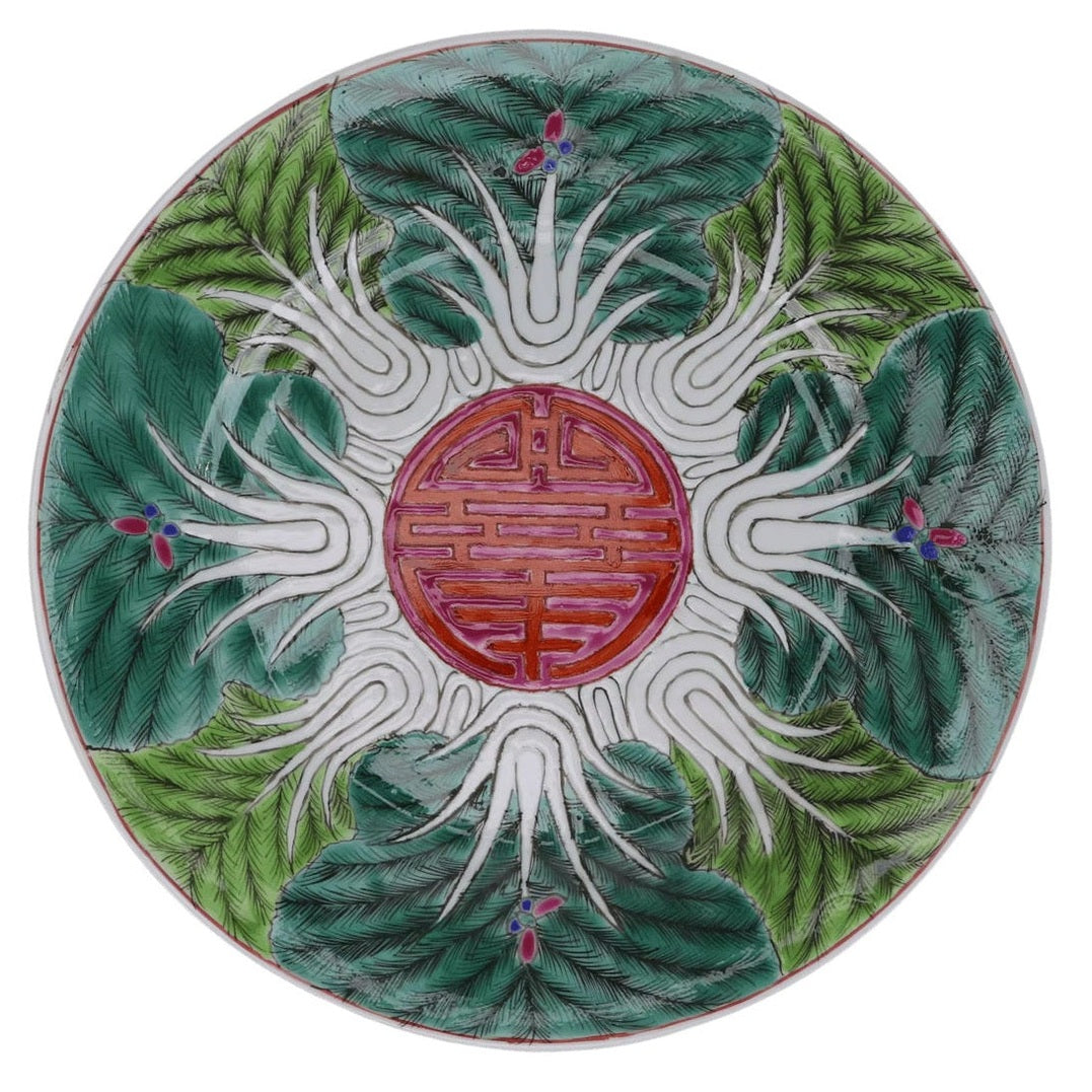 Decorative ceramic plate with green leaf design and red central emblem on a white background