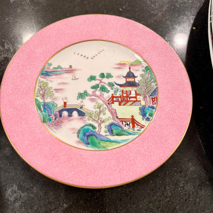 Decorative plate with a pink rim and scenic design on a dark surface
