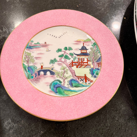 Decorative plate with a pink rim and scenic design on a dark surface